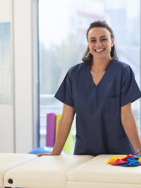 Portrait of happy female caucasian physiotherapist wearing scrubs at hospital. Hospital, physiotherapy, work, medicine and healthcare, unaltered.